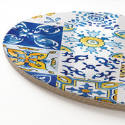 A close-up of a round wooden serving board featuring a blue-and-yellow watercolour Lisbon tile print, showing the stacked wood-like edge along the left side on a white background.