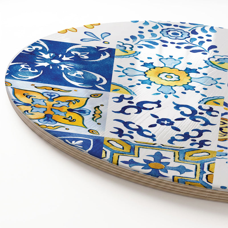 A close-up of a round wooden serving board featuring a blue-and-yellow watercolour Lisbon tile print, showing the stacked wood-like edge along the left side on a white background.
