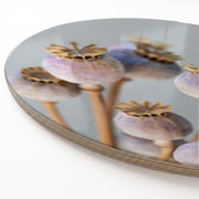 A close-up of a round wooden serving board featuring a purple giant poppy seed bunch print.