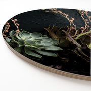 A round wooden serving board featuring a close-up photograph of succulent plants on a dark, textured background, set at an angle against a white studio backdrop.