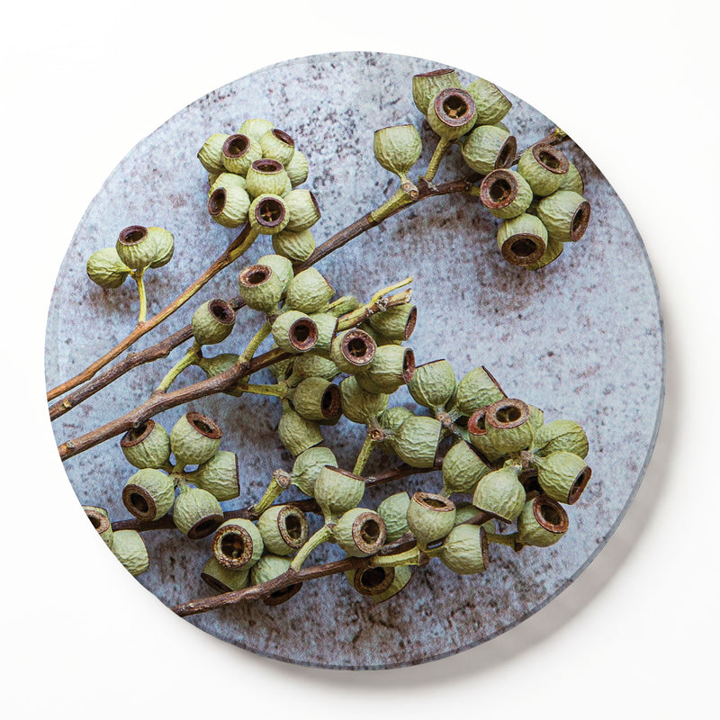 Round wooden serving board featuring a green natural ambernut print, shown against a plain white wall.