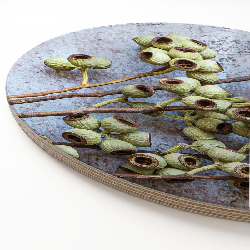 A round wooden serving board featuring a green natural ambernut print, shown at an angle on a white surface.