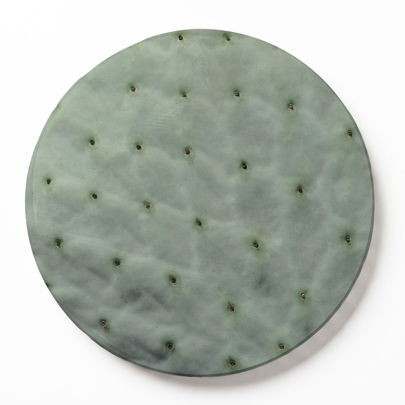A round wooden serving board featuring a green prickly pear leaf print, photographed from directly above on a white background.