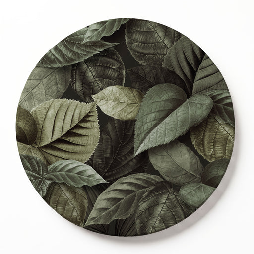 A round wooden serving board featuring an all-over monochromatic green botanical leaf print, shown against a plain white studio backdrop.