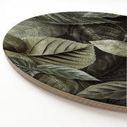 A round wooden serving board featuring an all-over monochromatic green botanical leaf print, shown on a clean white background.