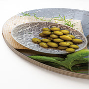 A round wooden serving board featuring a silver salt shaker and a green olive plate print against a white background.
