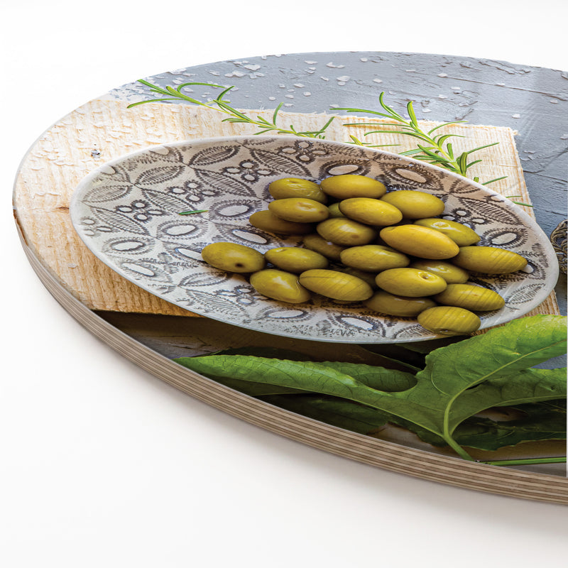 A round wooden serving board featuring a silver salt shaker and a green olive plate print against a white background.