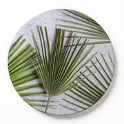 Round printed serving board featuring a green palm leaf pattern on a textured light grey background, shown as a circular wooden serving board with a subtle drop shadow on a white background.