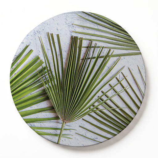 Round printed serving board featuring a green palm leaf pattern on a textured light grey background, shown as a circular wooden serving board with a subtle drop shadow on a white background.