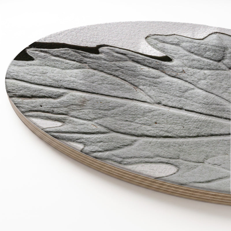 A round wooden serving board featuring a grey monochrome leaf print, shown on a clean white background.