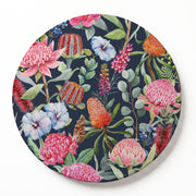 A round printed serving board featuring a vibrant tropical floral pattern with pink, red, and blue flowers on a dark navy background, shown on a clean white surface.