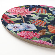 A round wooden serving board featuring a vibrant floral print with pink, red, and blue flowers on a dark navy background, photographed on a clean white surface.
