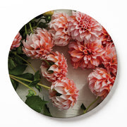 A round wooden serving board featuring a photographic print of pink and orange dahlias with green leaves, shown on a clean white background.