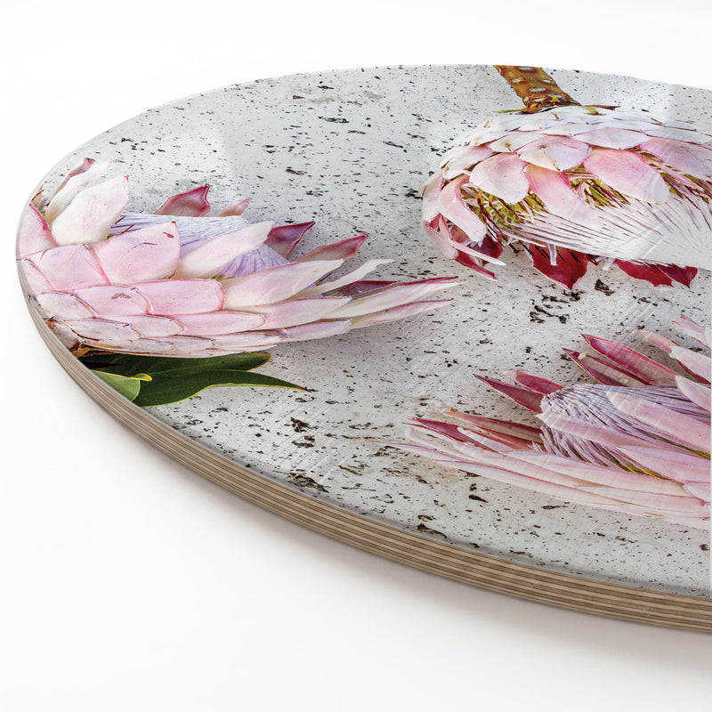 A round printed serving platter featuring a printed photographic design of pink protea flowers on a speckled light grey surface, shown on a clean white background.