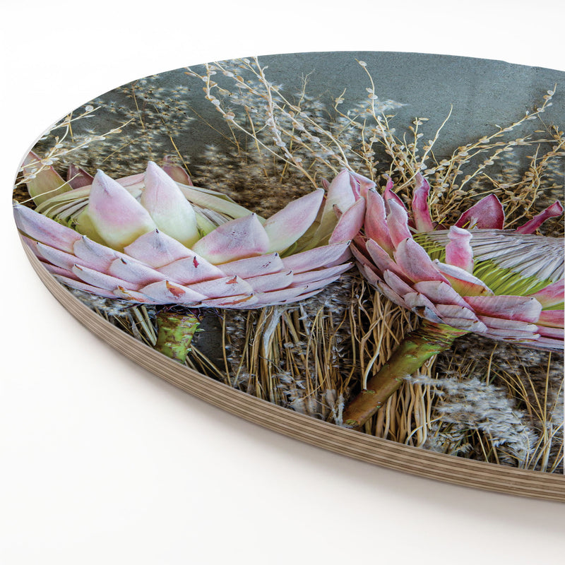 A round printed serving board featuring a close-up photograph of pink protea flowers and dried grasses against a white background.