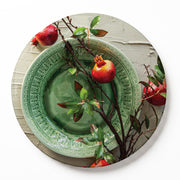 A round wooden serving board featuring a red pomegranate on a green plate print, set against a white background.