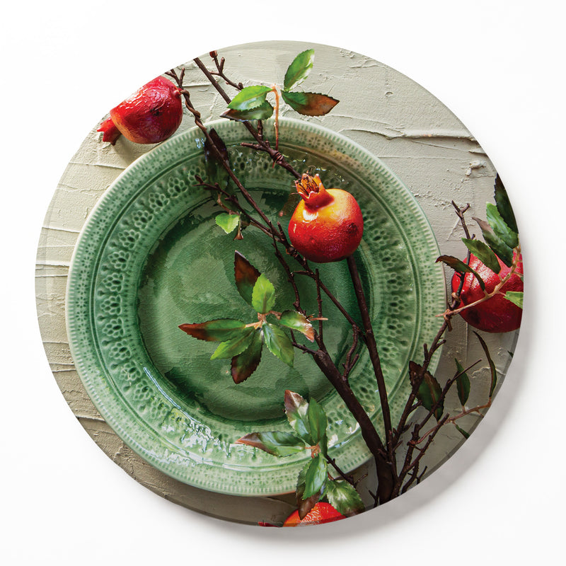 A round wooden serving board featuring a red pomegranate on a green plate print, set against a white background.
