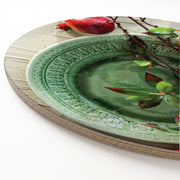 A close-up of a round wooden serving board featuring a red pomegranate on a green plate print.