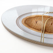 A close-up of a round wooden serving board featuring a beige wheat-on-wood print, photographed on a clean white background.