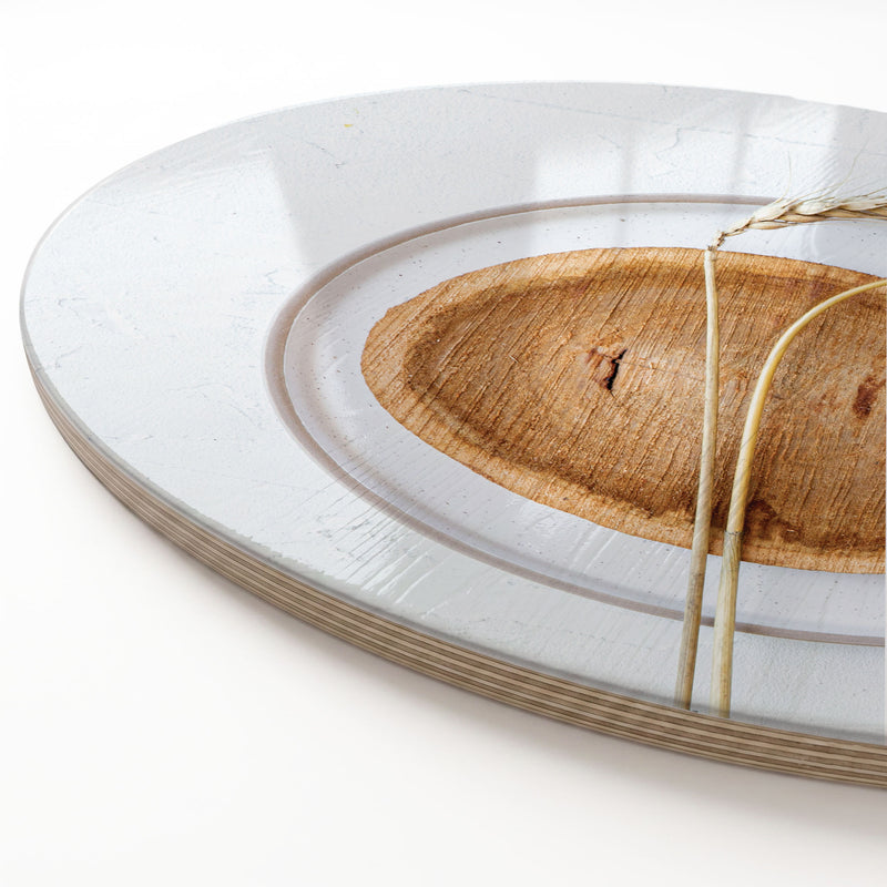 A close-up of a round wooden serving board featuring a beige wheat-on-wood print, photographed on a clean white background.