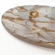 A close-up of a round wooden serving board featuring a bleached cream hydrangea floral pattern in warm tan and white tones, photographed on a clean white background.